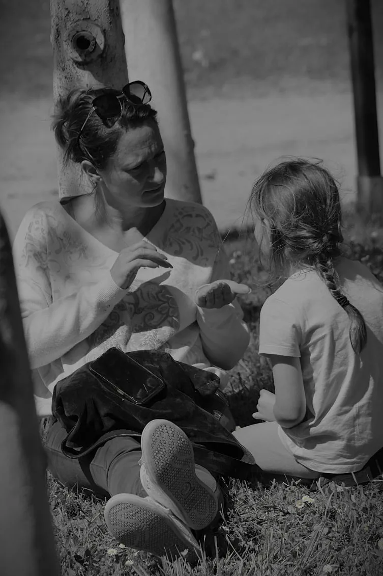 Une praticienne explique un geste à une petite fille, assises dans l'herbe